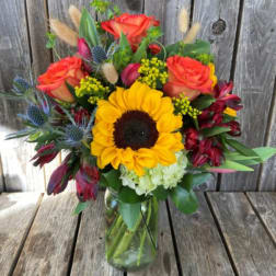 Bouquet of sunflowers, orange roses, and burgundy blooms in a glass vase