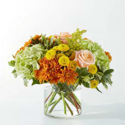 Bouquet of orange and yellow flowers with pale pink roses in a clear glass vase