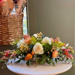 Low floral centerpiece with cream roses, peach blooms, and pink accents
