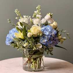 Blue hydrangeas and pale roses arranged in a clear glass vase