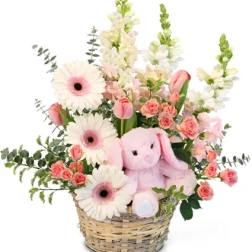 Pink and white flowers in a wicker basket with a plush bunny