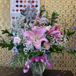 Pink lilies and roses in a glass vase with a pink ribbon