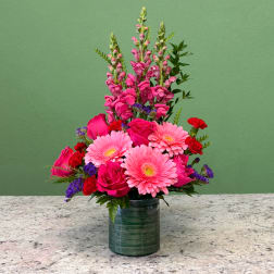 Tall pink floral arrangement with gerbera daisies, roses, and snapdragons in a green glass vase