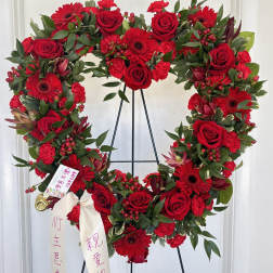 Large red floral heart wreath on a black stand with ribbon streamers.
