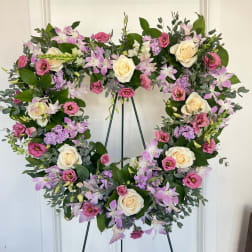 Heart-shaped floral wreath with pink, lavender, and cream blooms on a stand