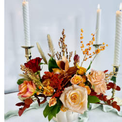 Autumn floral centerpiece with roses in a white vase and lit candles