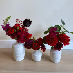 Three red and magenta flower arrangements in white ceramic vases
