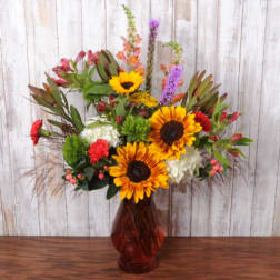 Mixed bouquet with sunflowers, red blooms, and white flowers in a red vase
