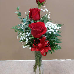 Three red roses in a clear glass vase with baby's breath and a red ribbon