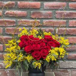 Red roses arranged with yellow filler flowers in a black vase