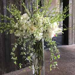 Tall white floral arrangement in a clear glass vase with trailing ivy