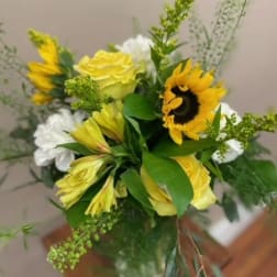 Bouquet of yellow roses, sunflowers, and white blooms in a glass vase