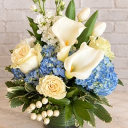 White calla lilies, cream roses, and blue hydrangeas in a green vase