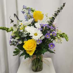 Bouquet of yellow roses, white daisies, and purple asters in a glass vase