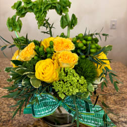 Yellow roses in a glass vase with green berries and foliage