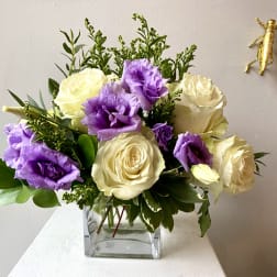 Bouquet of cream roses and purple lisianthus in a clear square vase