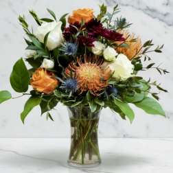 Bouquet of orange, white, and burgundy flowers in a clear glass vase