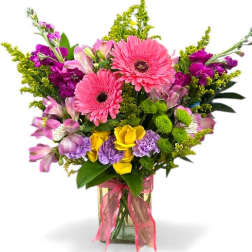 Mixed bouquet of pink gerbera daisies, purple flowers, and yellow roses in a glass vase