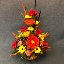 Autumn floral arrangement with gerbera daisies, carnations, and a small pumpkin in a vase