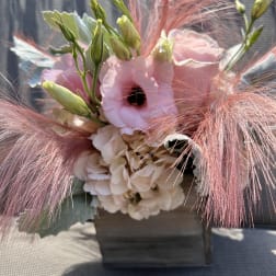 Pink and white floral arrangement with feathery pink accents in a wooden container