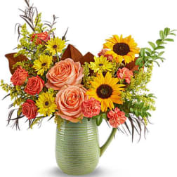 Bouquet of roses, sunflowers, and carnations in a green pitcher vase
