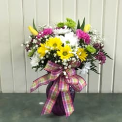 Colorful mixed flower arrangement in a purple vase with a plaid ribbon