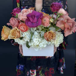 Colorful arrangement of roses and ranunculus with white hydrangeas in a white rectangular box.
