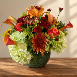 Mixed bouquet of orange, red, and green flowers in a dark glass vase