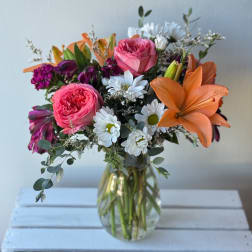 Bouquet of pink roses, orange lilies, and white daisies in a glass vase