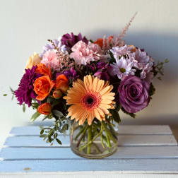 Mixed bouquet in a clear glass vase with purple, pink, orange, and peach flowers
