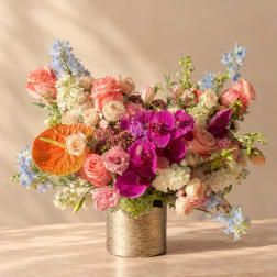 Mixed bouquet of pink roses, orchids, and blue flowers in a gold vase