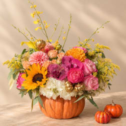 Colorful flower arrangement in a pumpkin-shaped container with small pumpkins nearby