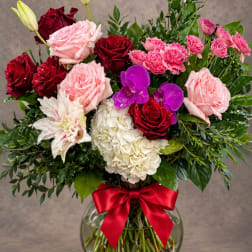 Mixed bouquet of pink and red roses with orchids in a glass vase