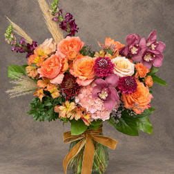 Mixed bouquet of orange and pink flowers in a glass vase with a ribbon