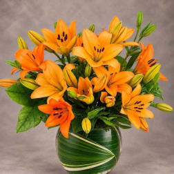 Orange lilies arranged in a round glass vase