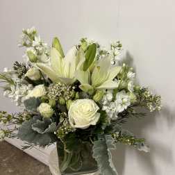 White lilies and roses arranged in a glass vase with silver foliage