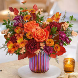 Orange roses and mixed fall flowers in a striped glass vase