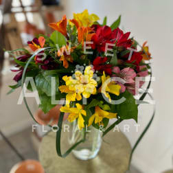 Mixed bouquet of red, yellow, orange, and pink flowers in a clear glass vase
