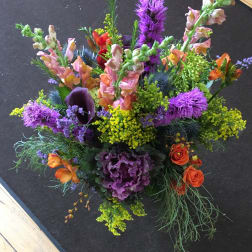 Tall mixed arrangement with purple, yellow, and orange flowers including snapdragons and roses
