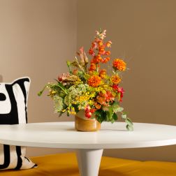 Colorful mixed flower arrangement in a gold vase on a white table
