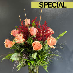 Peach roses arranged in a glass vase with red filler flowers