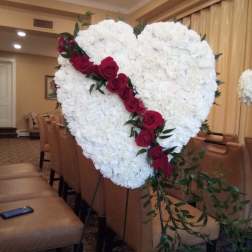 Heart-shaped white floral arrangement with red roses on an easel