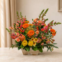 Mixed bouquet of orange, pink, and yellow flowers in a wooden container