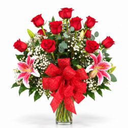 Red roses and pink lilies in a glass vase with a red bow