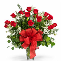 Red roses in a clear glass vase with a large red bow