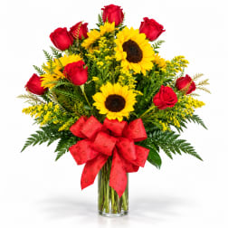 Bouquet of red roses and yellow sunflowers in a clear glass vase with a red bow