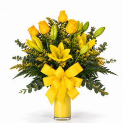 Yellow roses and lilies in a glass vase with a yellow bow