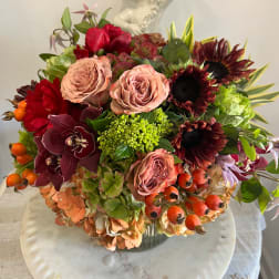 Mixed bouquet with roses, sunflowers, orchids, and berries in a glass vase