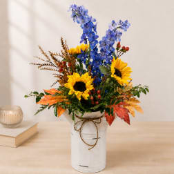 Blue and yellow floral arrangement in a white metal container with a bow