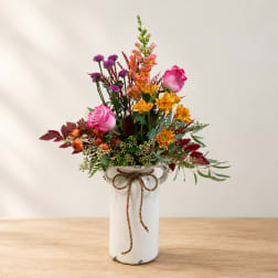 Pink roses and mixed flowers arranged in a white vase with a bow